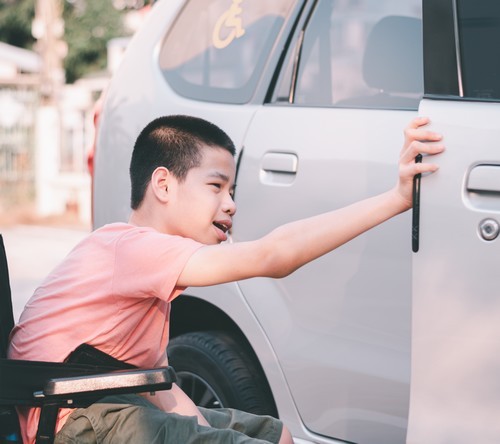 Aziatisch jongetje in rolstoel opent autodeur