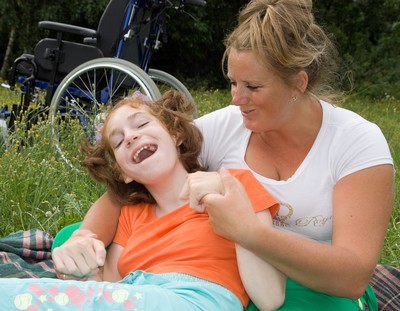 jong vrolijk meisje met handicap samen met assistente in het gras
