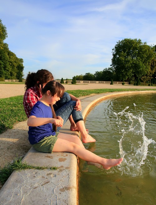 jong kind aan de rand van een fontein samen met haar mama