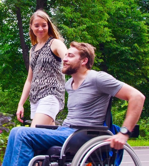 jongeman met handicap in rolstoel wandelt samen met vrouw in het park